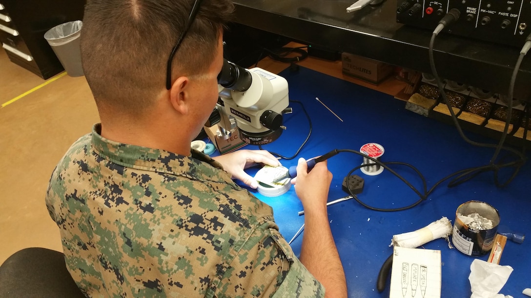 The Micro/Miniature Repair Course requires a steady hand and calm nerves in order to perform the necessary repairs on equipment.  Marines learn to perform component level repair on electronic components as small as one millimeter wide. Here, Lance Corporal Asencio, Jonathan R. performs eyelet repair under the watchful eye of his seasoned instructor, Staff Sergeant Cales, Noah M.  