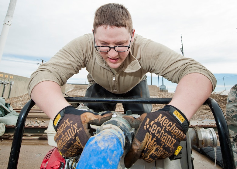 Senior Airman Matthew Singer, 91st Missile Maintenance Squadron electromechanical team technician, removes a hose from a water-pump near Bowbells, N.D., March 29, 2017. The electromechanical team technicians measured rising water levels and relocated water, snow and mud away from critical 91st MW assets. (U.S Air Force photo/Senior Airman J.T. Armstrong)