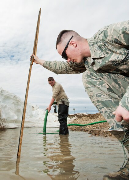 (From right) Airman 1st Class Heath Rauch and Senior Airman Matthew Singer, 91st Missile Maintenance Squadron electromechanical team technicians, measures and remove flood-water near Bowbells, N.D., March 29, 2017. Rauch and Singer worked with to drain water to a safe level. (U.S Air Force photo/Senior Airman J.T. Armstrong)