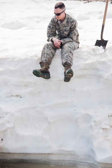 Airman 1st Class Heath Rauch, 91st Missile Maintenance Squadron electromechanical team technician, sits atop a snowbank above flood-water at a launch facility near Bowbells, N.D., March 29, 2017. Rauch was a part of a two-man team responsible for relocating flood-water away from critical assets at the launch facility. (U.S Air Force photo/Senior Airman J.T. Armstrong)