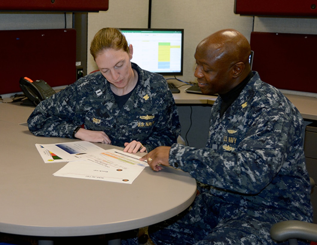 Defense Logistics Agency Aviation’s Navy Lt. Traci Irby, left, weapon system support program manager for the F/A-18, Navy Customer Facing Division,discuss metrics with Navy Cmdr. Eric Lockett, right, executive operations officer in the Customer Operations Directorate. Irby received an exceptional meritorious service award in a ceremony Mar. 13, 2017 for her performance during a 4-month assignment to Fleet Readiness South West at San Diego, California. Her performance while on assignment led to implementing Deputy Materiel Management Chief military positions to be placed at each of the FRC sites.