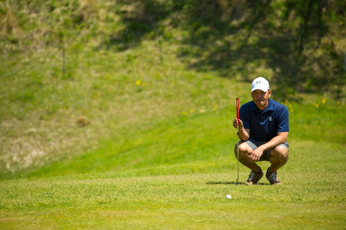 A participant in the 4th Annual Active-Duty Fund Drive in support of the Navy-Marine Corps Relief Society Golf Tournament kneels over the green to determine the angle required to put the ball in the hole at the Iwakuni Country Club in Iwakuni City, Japan, April 28, 2017. The tournament raised funds for NMCRS, which provides emergency financial assistance to active-duty and retired Navy and Marine Corps personnel and their families. (U.S. Marine Corps photo by Pfc. Stephen Campbell)