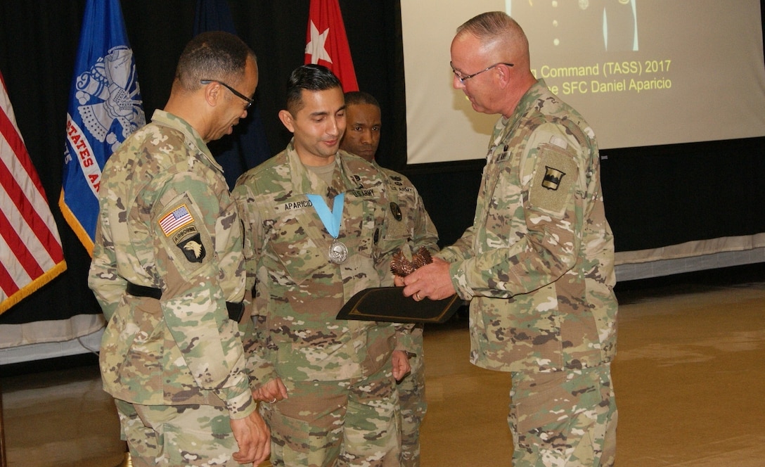 Sgt. 1st Class Daniel Aparicio (center) receives the Sgt. Audie Murphy Club Medal, Army Commendation Medal, and a bronze eagle from Maj. Gen. A.C. Roper (left), commander of the 80th Training Command, and Command Sgt. Maj. Jeffrey Darlington (right), the senior enlisted leader of the 80th TC, at the SAMC Induction Ceremony at Fort Devens, Massachusetts, April 6, 2017.