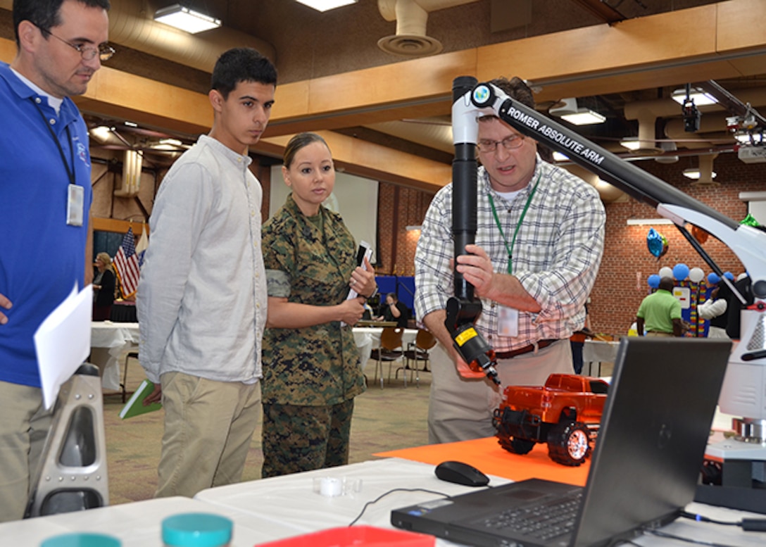 Demetrius McCray, a Manchester High School student looks on while Defense Logistics Agency Aviation engineering employees Aaron Vogt (blue shirt) and Kyle Hedrick (plaid shirt) demonstrate how to take a 3-dimensional scan of a red truck with a ROMER Absolute Arm with integrated scanner. 3-D imaging of parts is one method by which DLA Aviation is able to provide parts support for aging aircraft.  Demetrius McCray, stands next to his mother, Marine Corps Master Sgt. Olga Mcray, both of whom attended Defense Supply Center Richmond, Virginia’s, Take Your Daughters and Sons to Work Day on DSCR April 27, 2017.