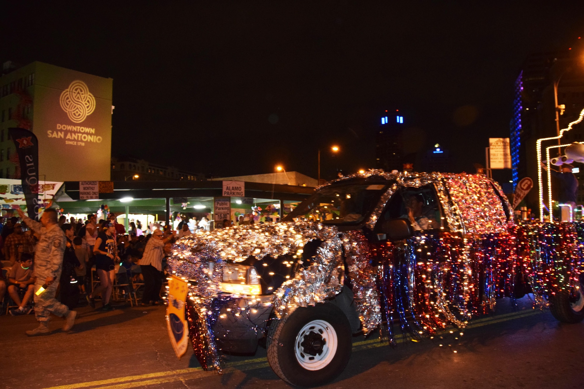 The 433rd Airlift Wing's “City Lights and Celebrations” themed float moves through downtown San Antonio during the 69th annual Fiesta Flambeau Parade, April 29, 2017,  passes a building illuminated with the logo symbolizing San Antonio’s tricentennial in 2018.  Over 700,000 spectators lined the 2.6 mile long route on the downtown streets of San Antonio to see over 200 floats and marching bands perform in the grand finale of Fiesta Week. (U.S. Air Force Photo/ Tech. Sgt. Carlos J. Trevino)