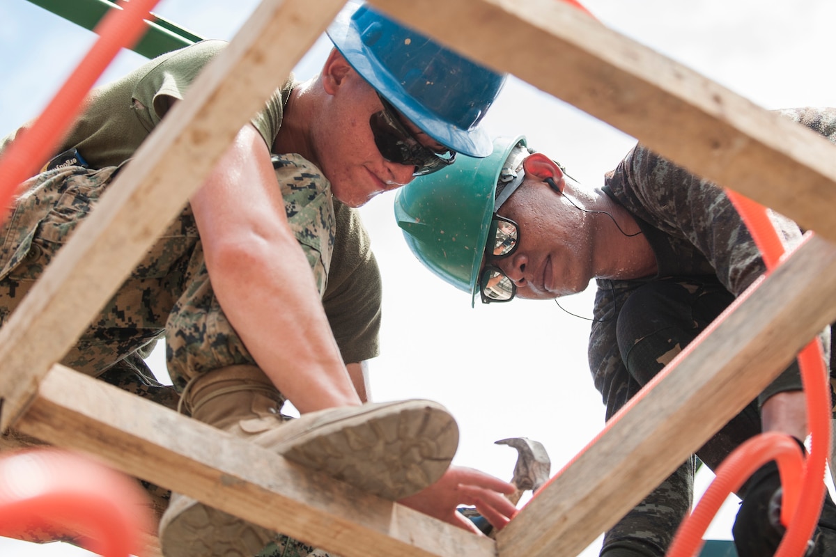A U.S. Marine and Philippine soldier install electrical wire casing in a new classroom.