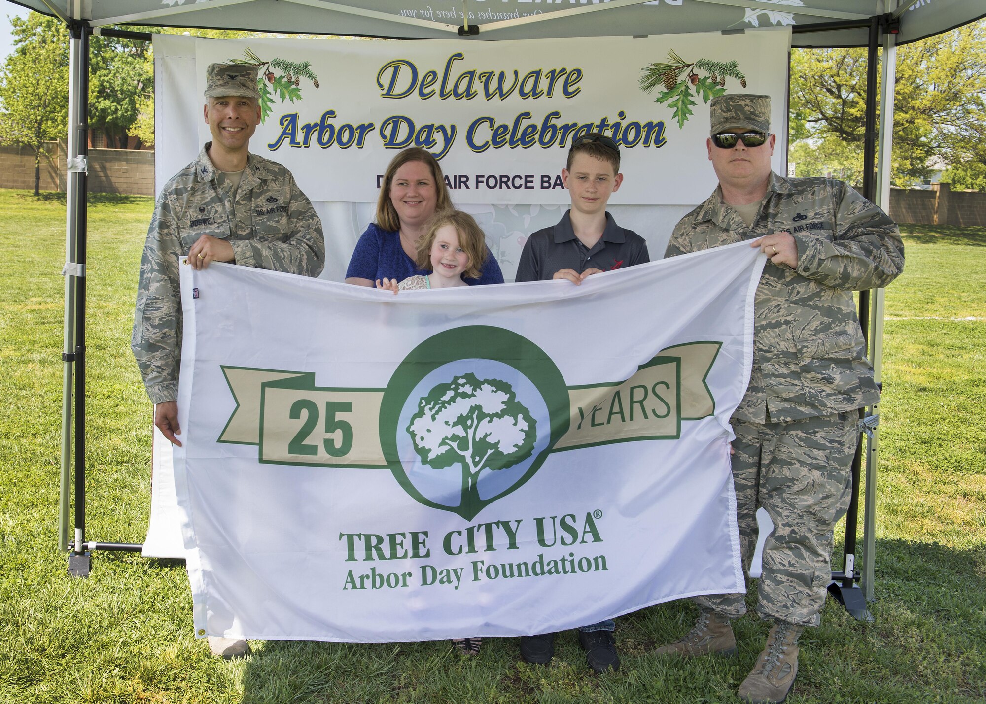 Col. Randy Boswell, 436th Mission Support Group commander, holds the Tree City USA flag with Master Sgt. Donald Bourne, 736th Aircraft Maintenance Squadron airframe power plant general section chief, and his family April 28, 2017, at Dover Air Force Base, Del. Bourne’s daughter, Audriana, won the Kindergarten-level for Kent County in an Arbor Day poster contest. (U.S. Air Force photo by Senior Airman Zachary Cacicia)