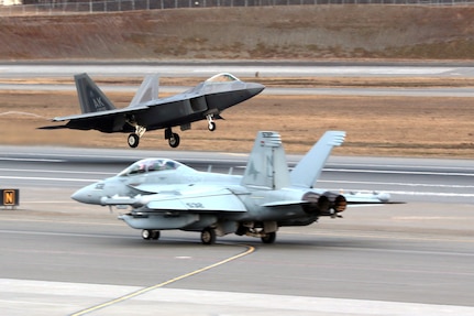 An Air Force 3rd Wing F-22 Raptor based here takes off while an F-18  E/F Carrier Strike Group 3, based out of Lemore Naval Air Station, California, taxis out to takeoff position on the first day of Exercise Northern Edge 17. Northern Edge is a biennial joint training exercise involving approzimately 6,000 personnel, that dates to 1975.