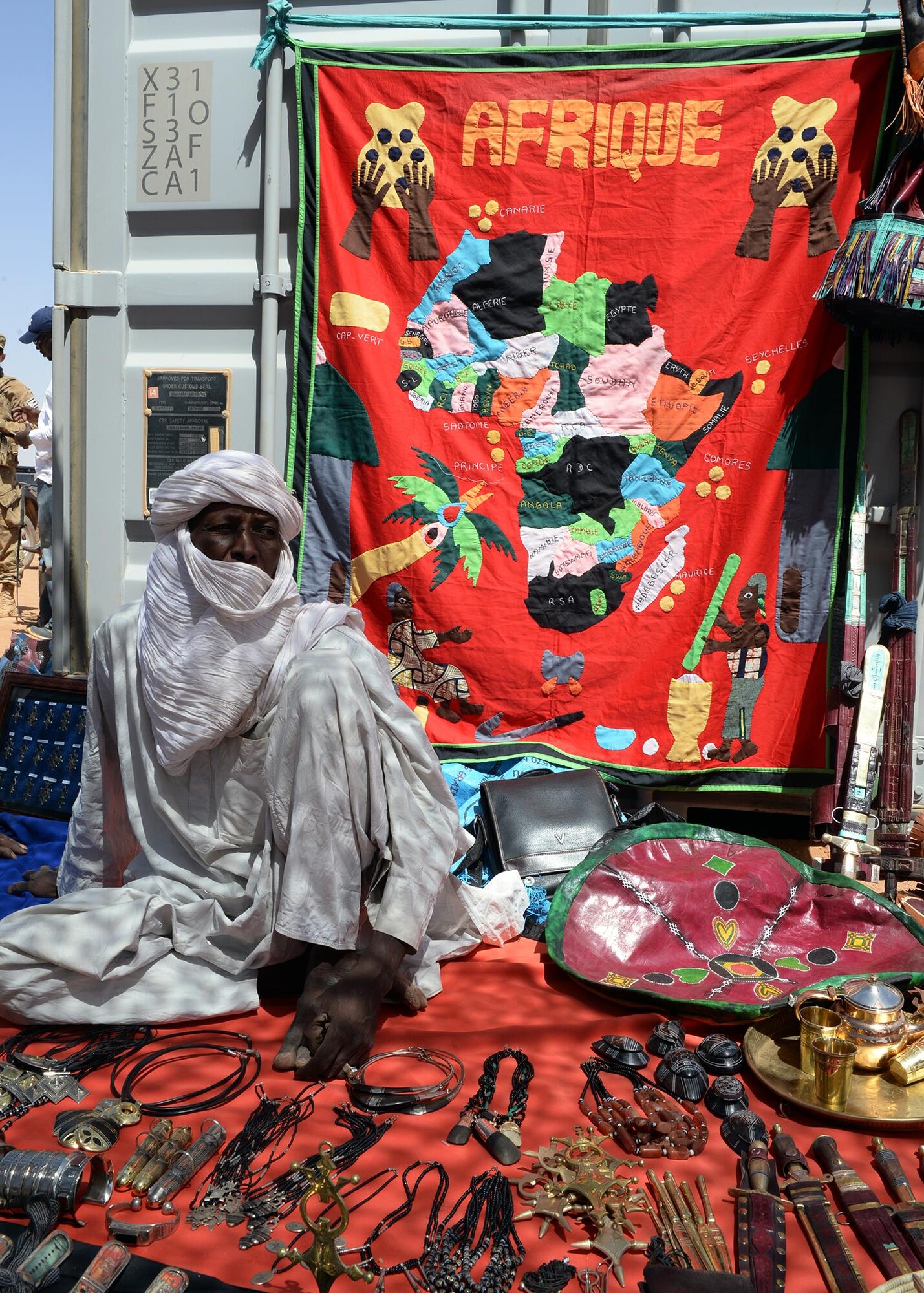 A merchant sits with his merchandise during a bazaar at Nigerien Air Base 201, Niger, April 16, 2017. More than 15 merchants participated in the bazaar, bringing local goods for Airmen to purchase as gifts and souvenirs. (U.S. Air Force photo by Senior Airman Jimmie D. Pike)