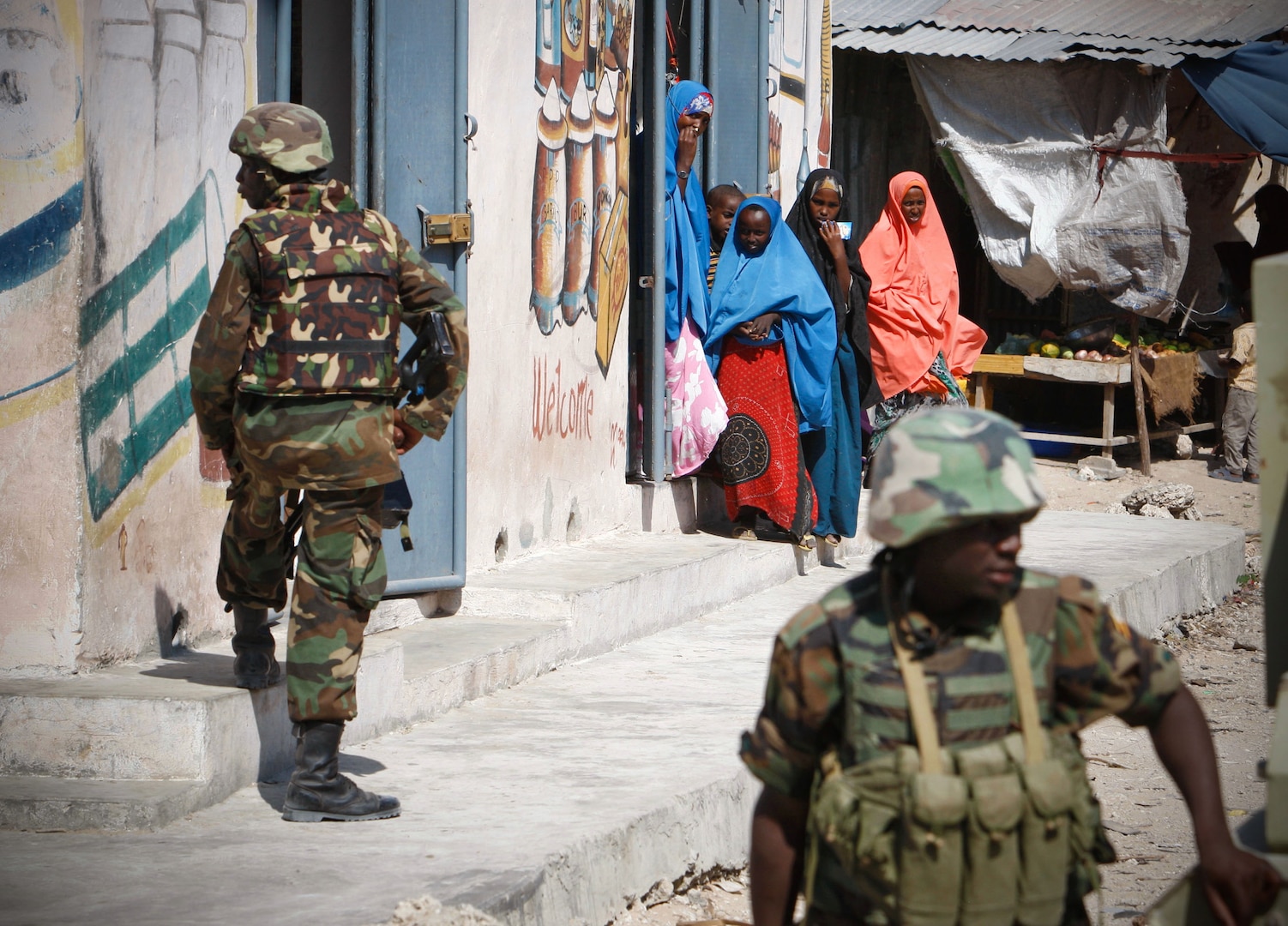 SOMALIA, Mogadishu: In a photograph taken 5 Dec and released by the African Union-United Nations Information Support Team 8 Dec, Somali women look on as Ugandan soldier serving with the African Union Mission in Somalia (AMISOM) take up defensive positions in Torfiq market in the Yaaqshid District of northern Mogadishu. In the face of a surge of car bombings and improvised explosive device (IED) attacks, the 9,700-strong African Union force continues to conduct security and counter-IED operations in and around the Somali capital. AU-UN IST PHOTO / STUART PRICE.