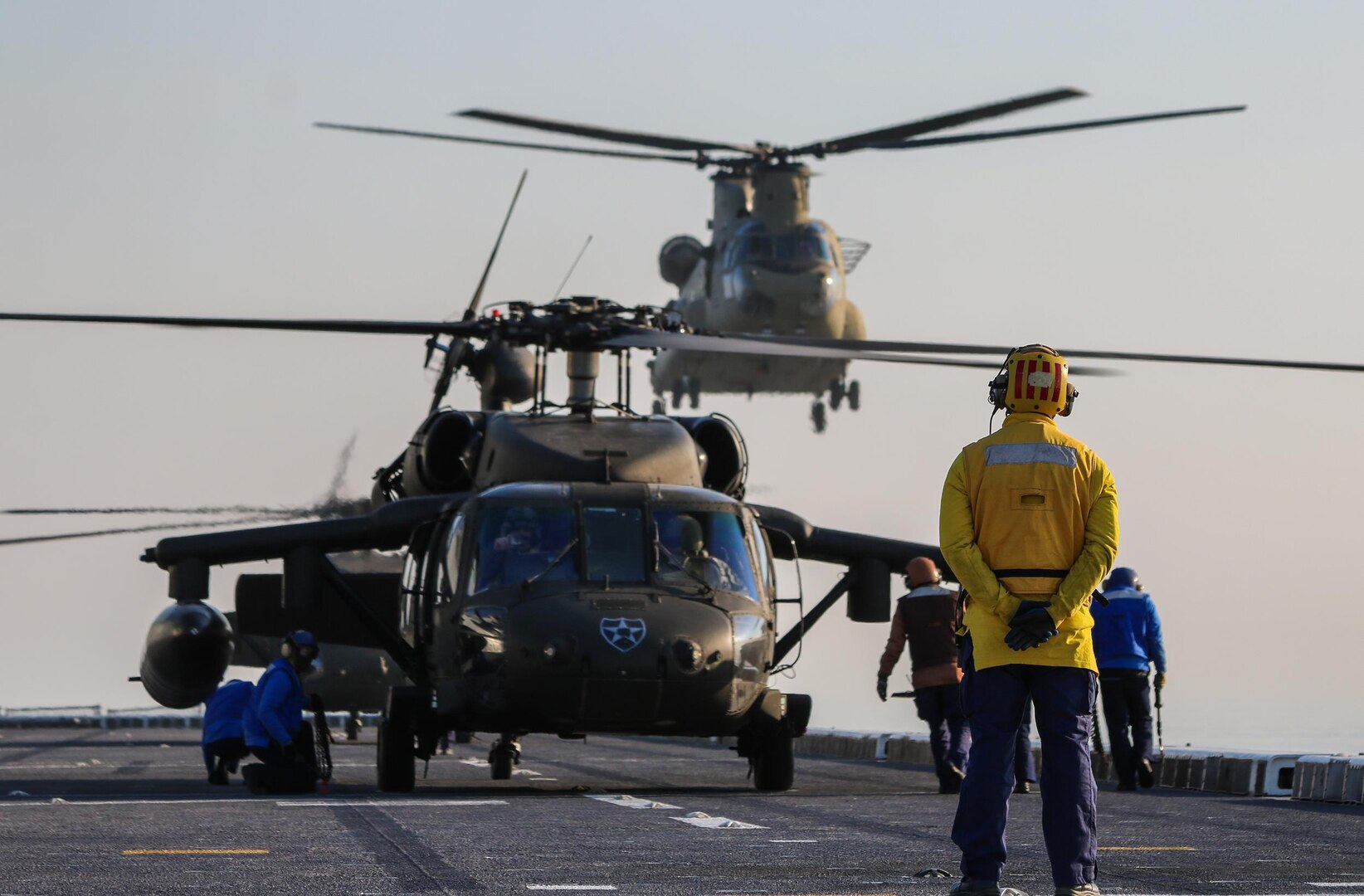 Aircrews from the 2nd Combat Aviation Brigade complete deck landing qualifications on the Republic of Korea Navy Ship Dokdo in the Yellow Sea last month. Here an ROK Navy air controller (right) watches a CH-47 Chinook from 3rd Battalion 2nd General Support Aviation Battalion approach the deck to land while ROK crews move to place chock blocks on two 2-2 AHB "Wildcard" Battalion Blackhawks. 