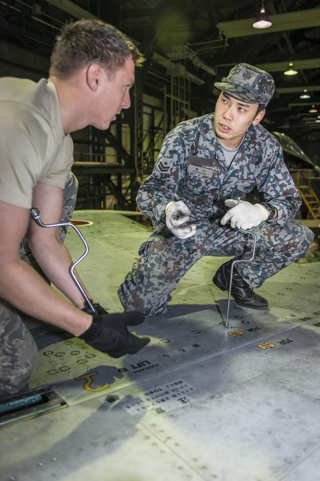 U.S. Air Force Staff Sgt. Jarrod Clark, left, a 35th Aircraft Maintenance Squadron crew chief, listens as his counterpart, Koku-Jieitai Airman 1st Class Koudai Okuguchi, right, a 2nd Air Wing Field Maintenance Squadron crew chief, explains how Koku-Jieitai maintainers care for their F-15J Eagles during a 10-day U.S.-Japan Bilateral Career Training at Chitose Air Base, Japan, April 18, 2017. Okuguchi and Clark worked together to remove a panel from the aircraft to conduct repairs before sending the jet back to the flight line for operational orders. Koku-Jieitai is the traditional term for Japan Air Self Defense Force used by the Japanese. (U.S. Air Force photo by Tech. Sgt. Benjamin W. Stratton)