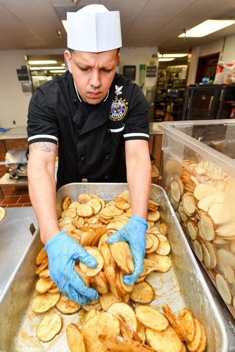 Navy culinary specialist Petty Officer 2nd Class Roel Caballero, assigned to Naval Base Kitsap-Bangor’s Trident Inn Galley, in Silverdale, Wash., seasons and mixes sliced potatoes for lunch, May 2, 2017. Navy photo by Petty Officer 3rd Class Charles D. Gaddis IV