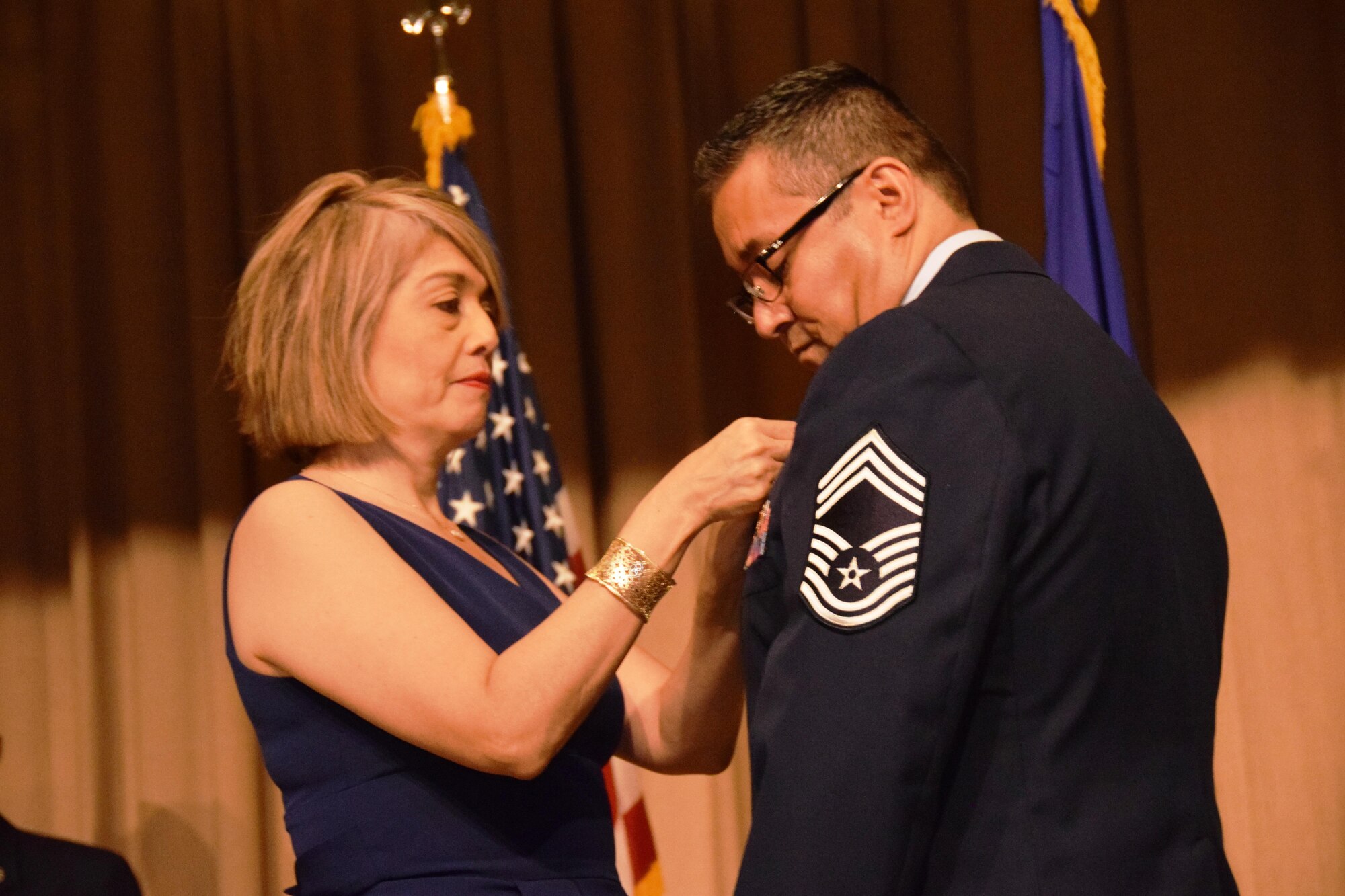 Chief Master Sgt. Christopher E. Florez  receives his retirement pin from his wife, Angelica, in the Wilford Hall Auditorium at Joint Base San Antonio-Lackland, Texas on May 7, 2017. (U.S. Air Force photo by Tech. Sgt. Carlos J. Trevino)