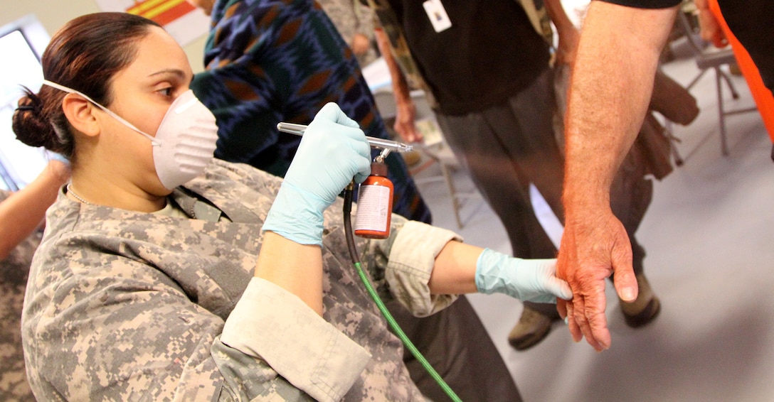 MUSCATATUCK URBAN TRAINING CENTER, Indiana – Spc. Lesymar Aviles from Sabana Grande, Puerto Rico, an ammunition stock control specialist with the 266th Ordnance Company, Aguadilla, Puerto Rico, sprays paint to simulate a burn wound onto a civilian volunteer at the Muscatatuck Urban Training Center (MUTC), Indiana, May 6, 2017. Nearly 4,100 Soldiers from across the country are participating in Guardian Response 17, a multi-component training exercise to validate U.S. Army units’ ability to support the Defense Support of Civil Authorities (DSCA) in the event of a Chemical, Biological, Radiological, and Nuclear (CBRN) catastrophe.