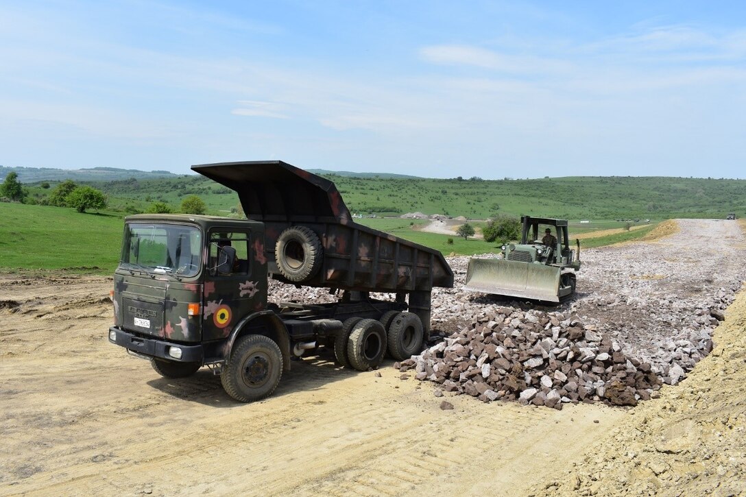 A soldier of the 10th Romanian Engineer Brigade places rock for a road on the Non-Standard Live-Fire Range at Joint National Training Center, Cincu, Romania, as part of Resolute Castle 17, while Spc. Jeffrey Nichols of the 381st Engineer Company, 926th Engineer Battalion, 926th Engineer Brigade, United States Army Reserves, stands by to bulldoze. Resolute Castle 17 is an exercise strengthening the NATO alliance and enhancing its capacity for joint training and response to threats within the region.