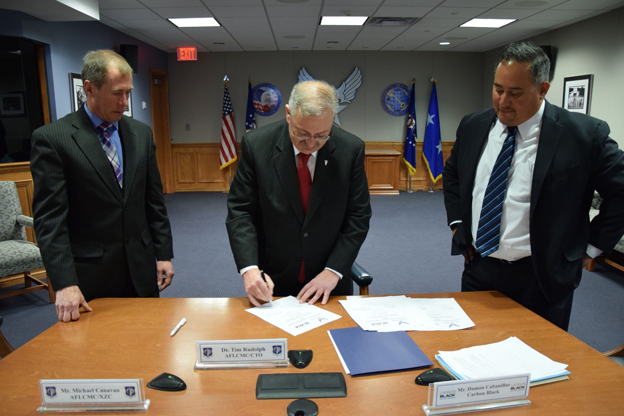 Dr. Tim Rudolph, center, former Air Force Life Cycle Management Center chief technology officer, signs the paperwork for a Cooperative Research and Development Agreement with Carbon Black, March 15 at Hanscom Air Force Base, Mass., while Michael Canavan, left,  Electronic Systems Development Division chief, and Damon Cabanillas, vice president of federal sales and operations, Carbon Black, look on. The Electronic Systems Development Division signed a CRADA with Carbon Black to enable deployment of advanced endpoint security technology on the Hanscom Collaboration and Innovation Center to improve cybersecurity.  (U.S. Air Force photo)