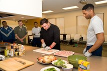 Team Dover members watch Robbie Jester, executive chef at the Stone Balloon Ale House, Newark, Del., demonstrates how to cut chicken for stir-fry May 5, 2017, at the Health Promotions Flight on Dover Air Force Base, Del. Jester, winner of Food Network’s “Beat Bobby Flay,” showed attendees how to make two different versions of chicken stir-fry at Dover’s Wingman University “Dorm to Gourm” class. (U.S. Air Force photo by Roland Balik)