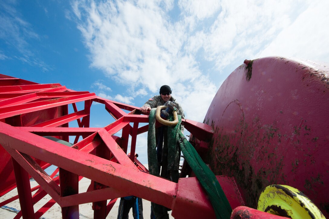 Connecticut Army National Guard Sgt. 1st Class Chris Richards attaches slings onto a 12,000-pound beached buoy in Chatham, Mass., May 9, 2017. The buoy was lifted from the beach by a CH-47 Chinook helicopter and dropped offshore where the U.S. Coast Guard Cutter Oak picked it up. Coast Guard photo by Petty Officer Andrew Barresi