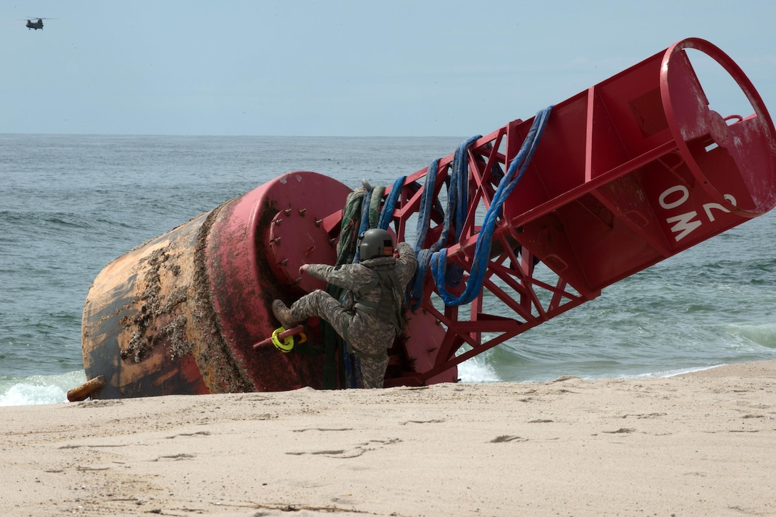 Connecticut Army National Guard Sgt. 1st Class Chris Richards prepares to climb atop a 12,000-pound beached buoy near Chatham, Mass., May 9, 2017. He attached the slings to a CH-47 Chinook helicopter which lifted the buoy from the beach. Coast Guard photo by Petty Officer 3rd Class Andrew Barresi