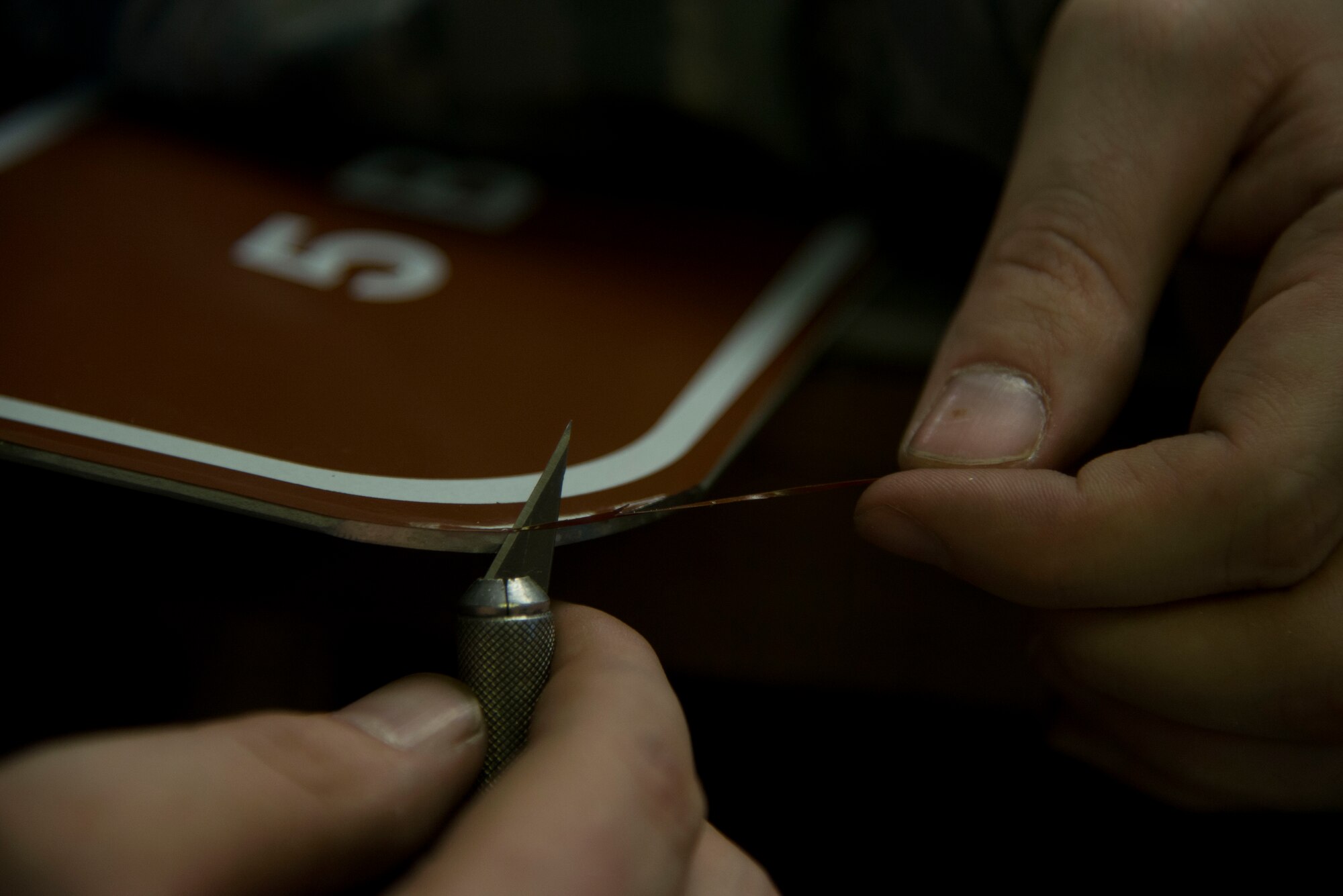 Staff Sgt. Horace Hand, 5th Civil Engineer Squadron structural craftsman, cuts excess vinyl from a sign at the sign shop on Minot Air Force Base, N.D., April 27, 2017. Hand uses a small sculpting knife to cut overlapping vinyl from the sign’s edges. (U.S. Air Force photo/Airman 1st Class Dillon Audit)