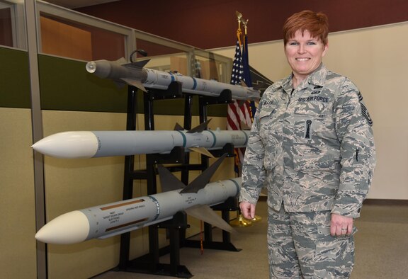 Oregon Air National Guard Chief Master Sgt. Kristen Miller pauses for a photograph next to a display of weapons in her work area at the 142nd Fighter Wing, Portland Air National Guard Base, Ore., May 7, 2017. Miller recently was appointed as the first female Chief Master Sergeant Munitions System Specialist Superintendent in the Air National Guard. (U.S. Air Force photo by Tech. Sgt. John Hughel)