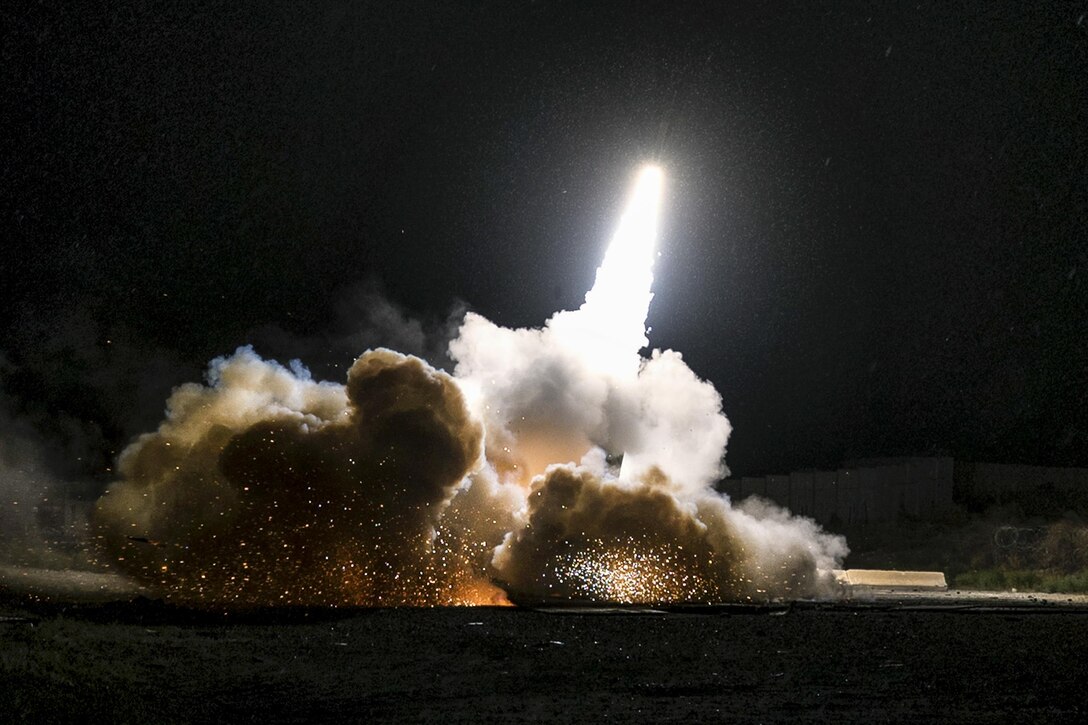 A rocket system launches, illuminating the night sky and creating sparks and smoke clouds.