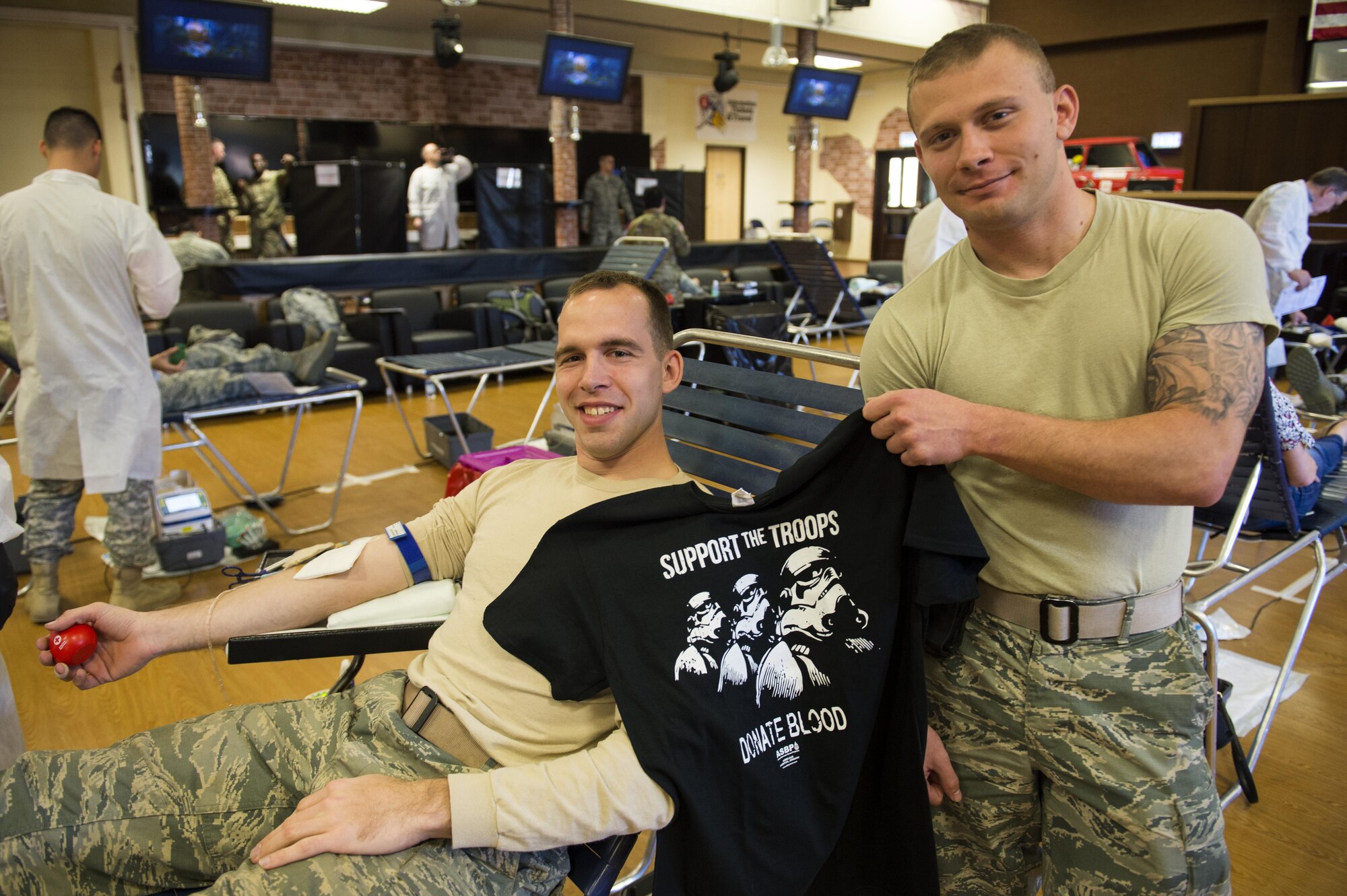 U.S. Air Force Airman 1st Class Ian Christner and Senior Airman Allen Turner, both 52nd Civil Engineer Squadron heavy equipment operators, pose with a Star Wars themed blood donor shirt during an Armed Services Blood Program blood drive in the Brick House at Spangdahlem Air Base, Germany, May 10, 2017. The ASBP is the official blood collection, manufacturing and transfusion program for the U.S. military.