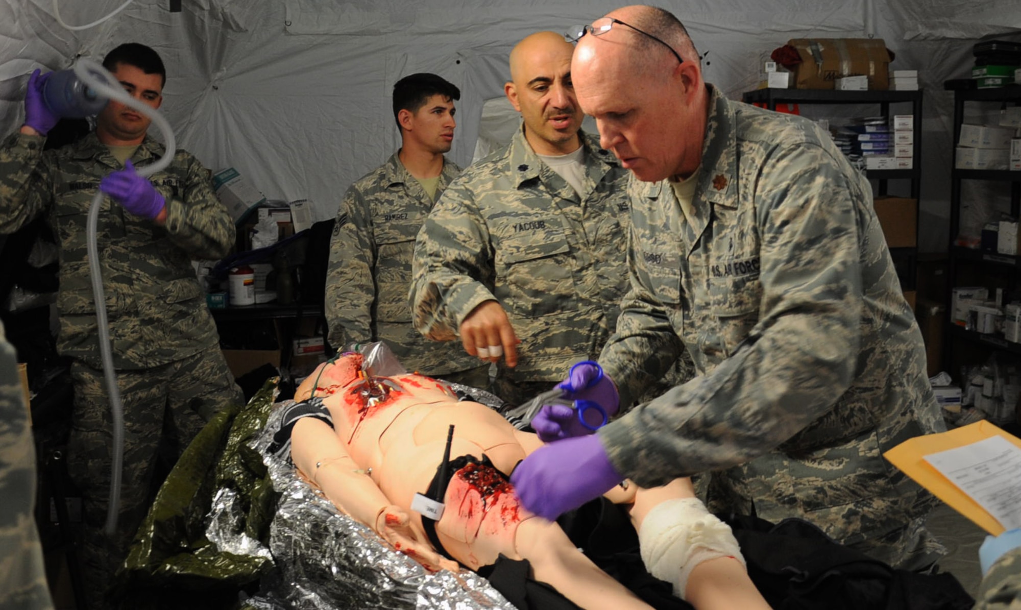 Maj. Richard Odosso (with scissors), 779th Medical Group nurse, cuts away the clothing of a dummy portraying a wounded patient at the group's Emergency Medical Support facility April 28, 2017 at Camp Atterbury, Ind. The patient showed wounds resulting from an electrical shock which threatened his kidneys. Once stabilized in the emergency room, he was transferred to the facility's intensive care unit for monitoring before being transferred again to the next level of care. (U..S. Air Force photo by Staff Sgt. Joe Yanik)
