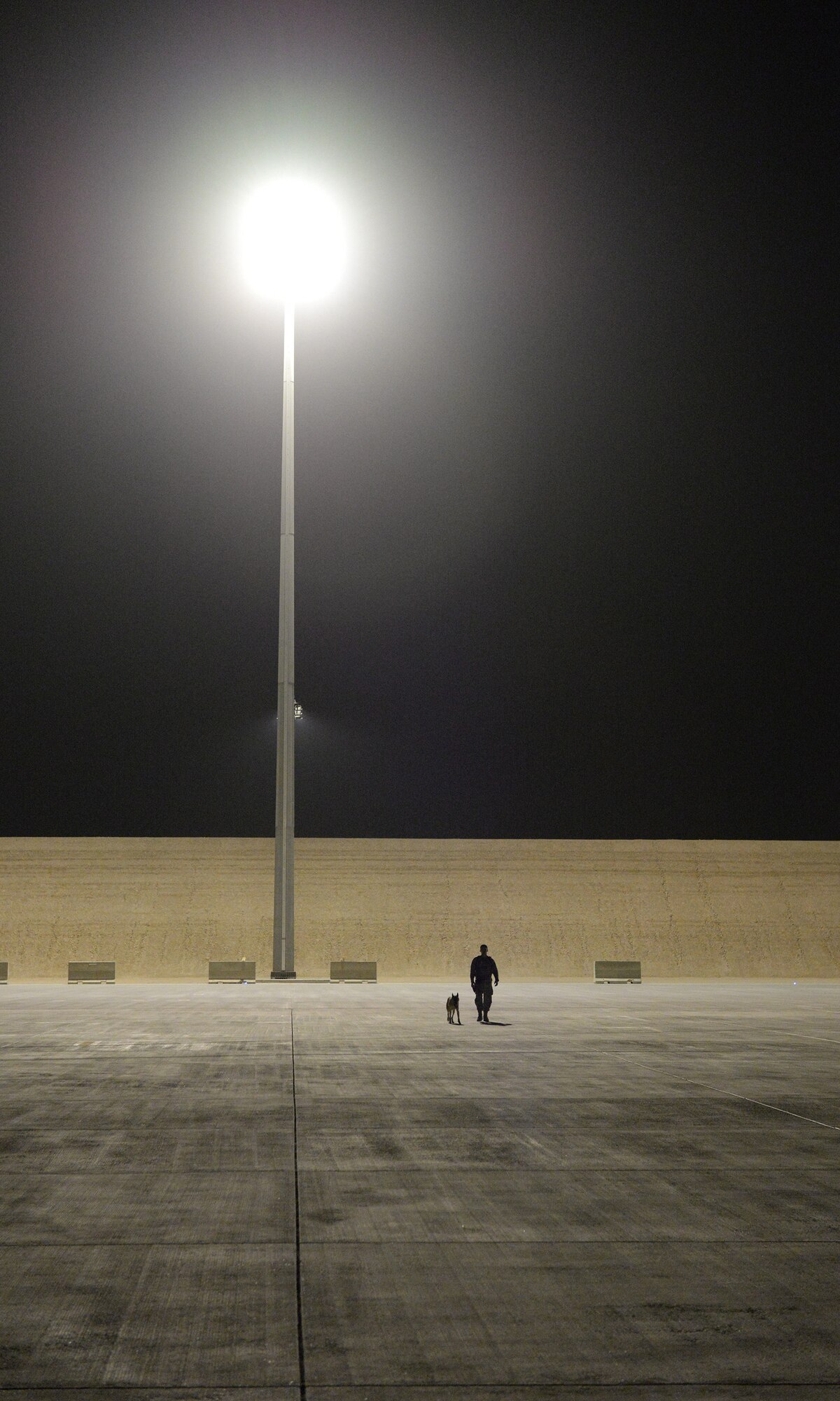 U.S. Air Force Staff Sgt. Louis Diaz-Garcia, a military working dog handler assigned to the 379th Expeditionary Security Forces Squadron, and his military working dog Roy take a walk under the runway lights at Al Udeid Air Base, Qatar, May 4, 2017. Diaz-Garcia and Roy are unwinding after participating in a detection exercise designed to give the K-9 teams an opportunity to familiarize themselves with the general layout and specific challenges associated with detection aboard an aircraft. (U.S. Air Force photo by Tech. Sgt. Bradly A. Schneider/Released)
