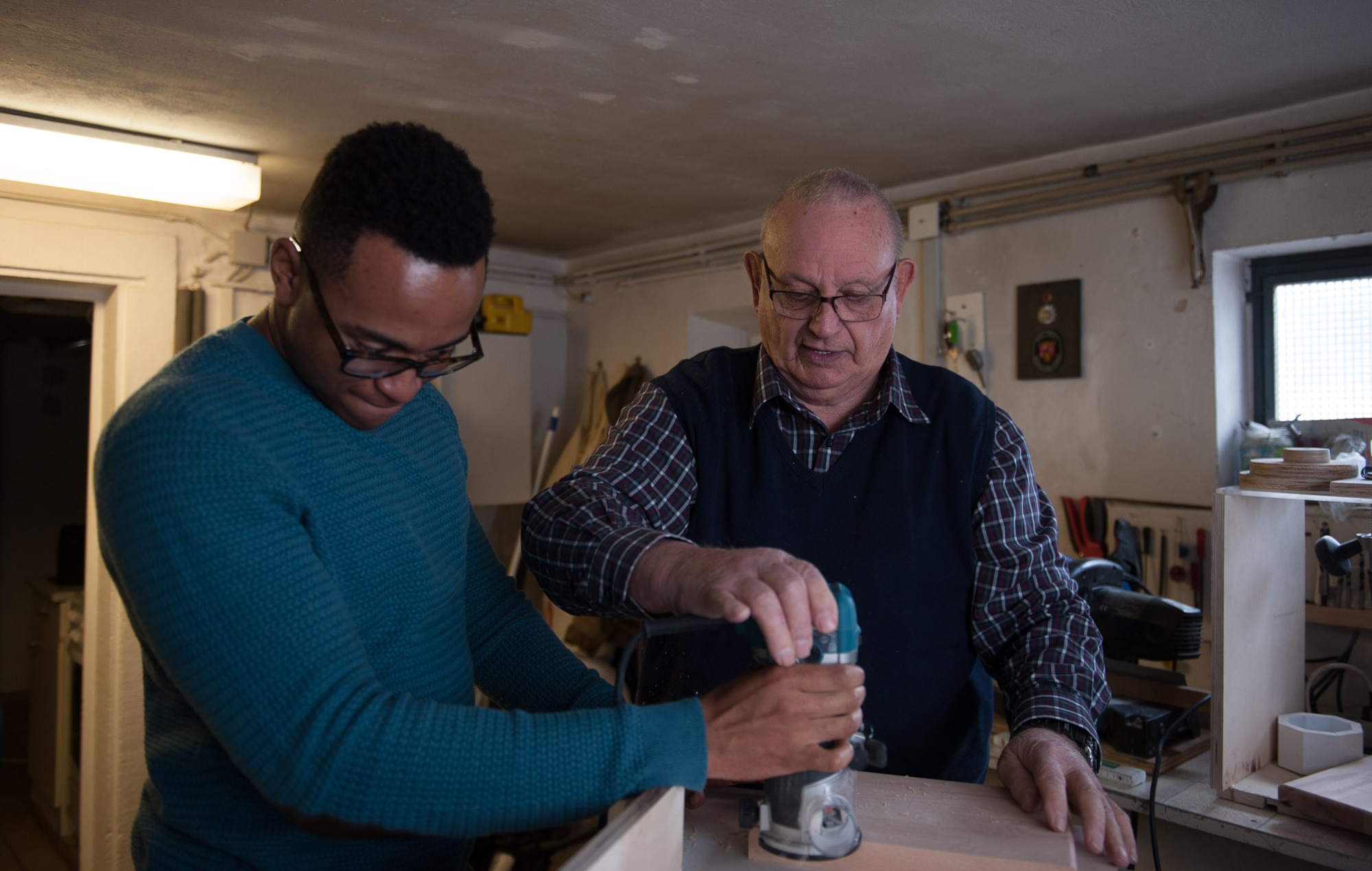 Retired Chief Master Sgt. Charles E. Milam shows Airman 1st Class Timmethy James, 86th Airlift Wing Public Affairs broadcaster, how to properly edge a piece of wood in his workshop in Waldfischbach-Burgalben, Germany, May 2, 2017.  During his 30 years of active-duty service, Milam was awarded the Bronze Star for his valor and meritorious service while he had administrative supervision over 11 Airmen assigned to security for the Presidential Advisor on Vietnam Affairs. He also trained Vietnamese guards who provided security for the embassy housing during his second Vietnam tour. (U.S. Air Force photo by Airman 1st Class Savannah L. Waters)