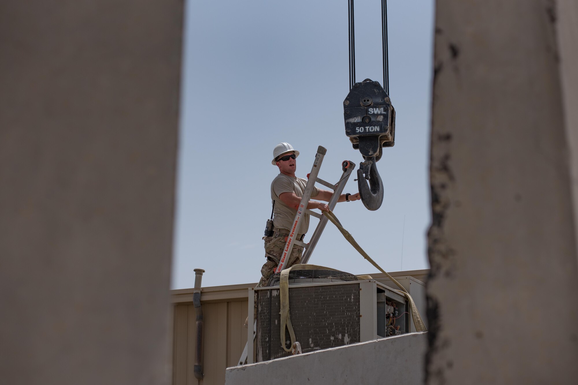 Staff Sgt. Matthew Sayward, a pavement equipment operator with the 407th Expeditionary Civil Engineer Squadron, guides a crane hook into place above a heating, ventilation and air conditioning unit May 4, 2017, in Southwest Asia. Sayward regular assists HVAC technicians during the move of multi-ton, AC package units on roofs and outdoor mounts. As average daily temperatures in the Air Force Central Command region of operations exceed 100 degrees Fahrenheit, cooling units are essential to support continuous missions of coalition forces against ISIS. (U.S. Air Force photo by Staff Sgt. Alexander W. Riedel)