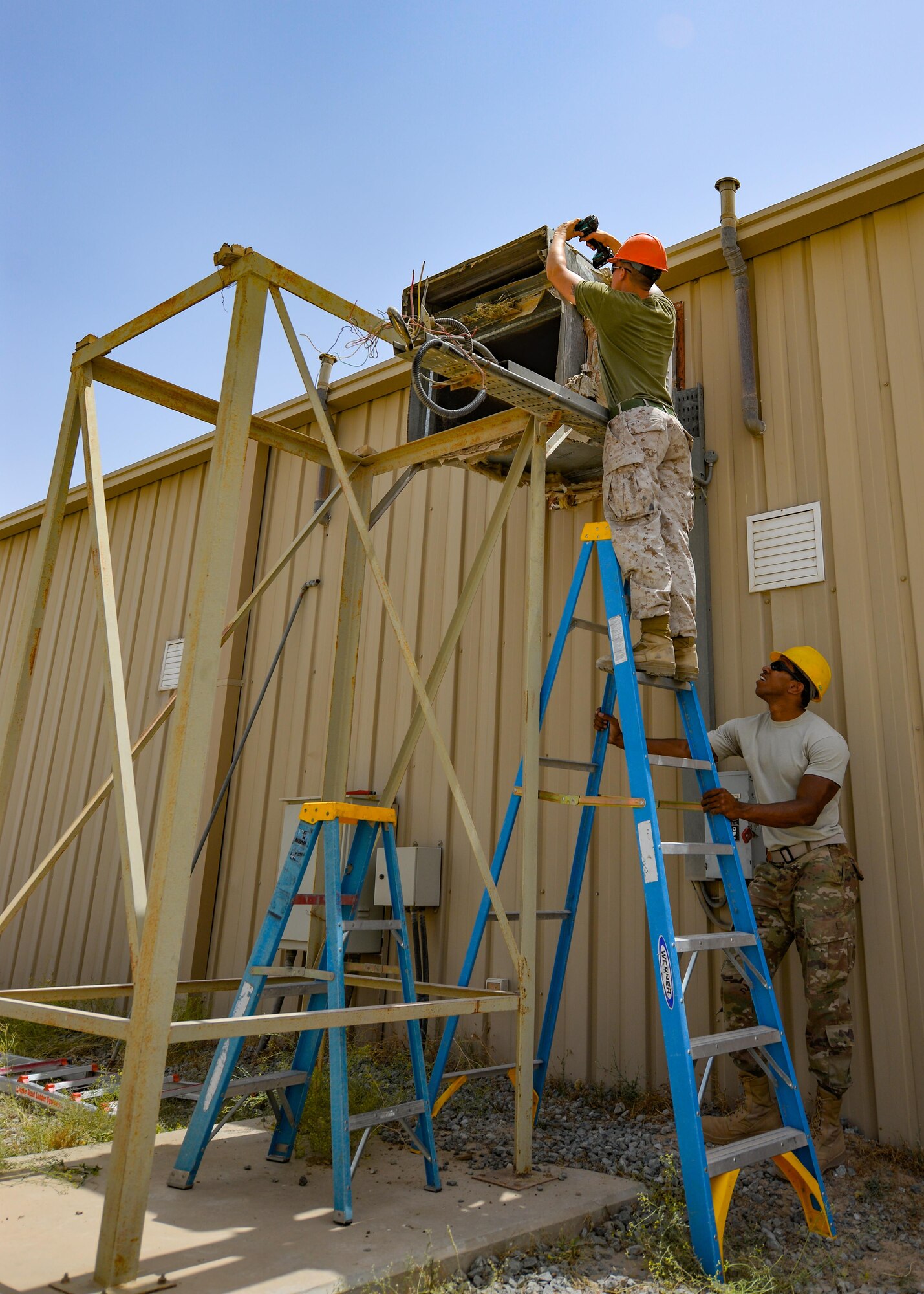 U.S. Marine Corps Sgt. Jospeh Spore, a welder with Marine Wing Support Squadron 372, top, prepares an air duct opening for the installation of a new industrial air conditioning unit while Staff Sgt. Hassan Mateyka, an HVAC technician with the 407th Expeditionary Civil Engineer Squadron, secures the ladder May 4, 2017, in Southwest Asia. Expeditionary Marines with MWSS 372 support the Group Special Purpose Marine Air-Ground Task Force-Crisis Response-Central Command, which is collocated with the 407th AEG. Marines and Airmen frequently partner to sharpen joint skillsets and complete pressing work assignments. (U.S. Air Force photo by Staff Sgt. Alexander W. Riedel)