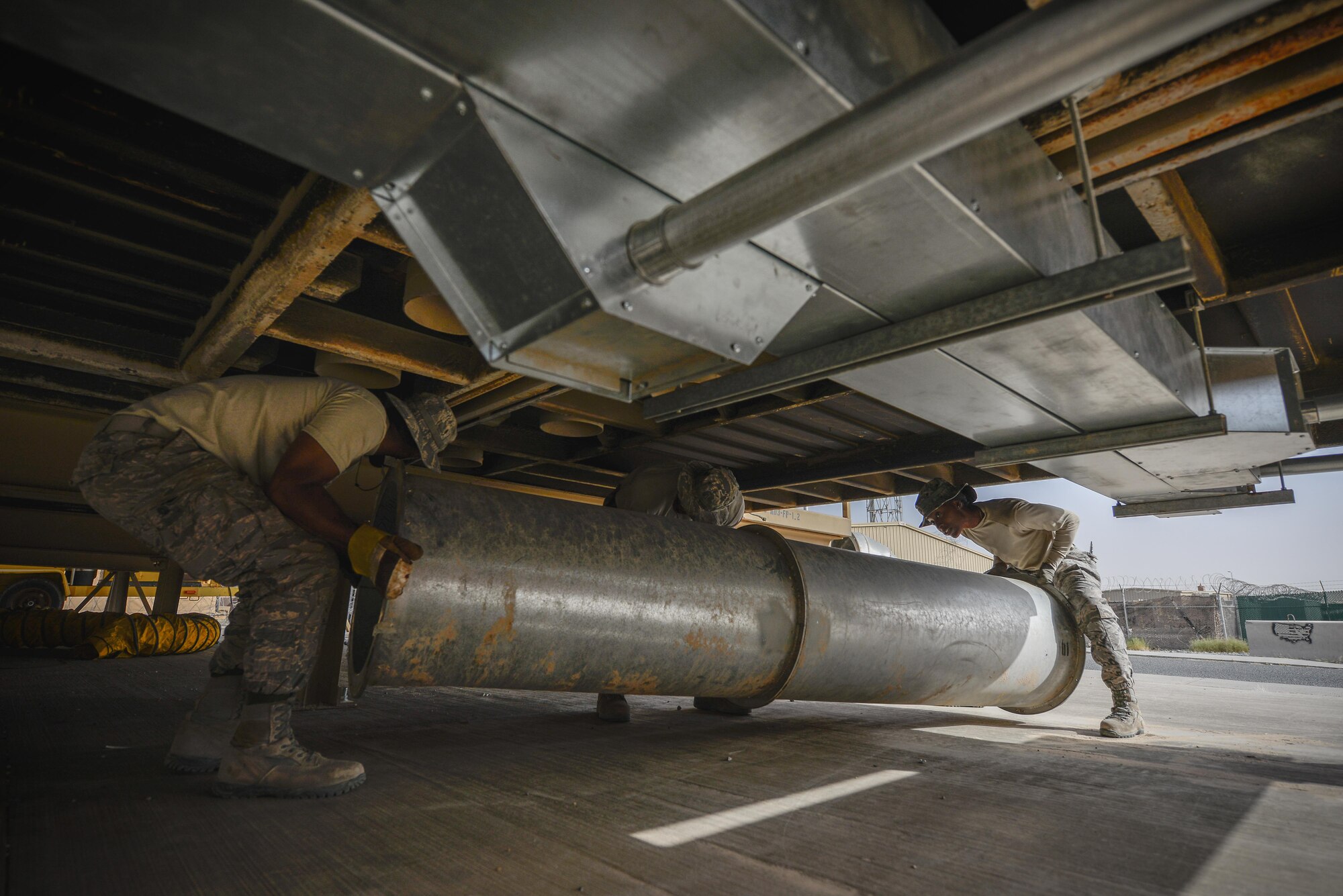 Senior Airman Jurel Burton, left, and Staff Sgts. Hassan Mateyka and Yavita Cotton,  heating, ventilation and air conditioning technicians with the 407th Expeditionary Civil Engineer Squadron, move a metal air-conditioning underneath a mobile trailer building May 4, 2017, in Southwest Asia. The team installed the ducts in confined space to increase air flow to cool vital computer systems inside. (U.S. Air Force photo by Staff Sgt. Alexander W. Riedel)