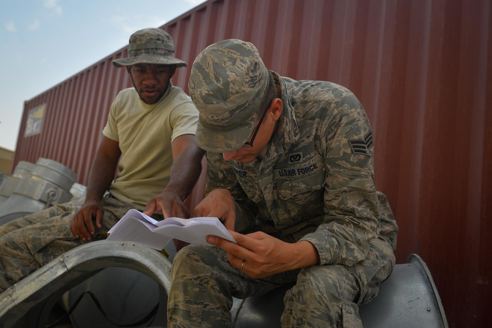 Senior Airmen Jurel Burton, left, and Cody Ewer, both heating, ventilation and air conditioning technicians with the 407th Expeditionary Civil Engineer Squadron, consult a construction plan during the installation of an air conditioning duct, May 4, 2017, in Southwest Asia. The new cooling system will provide cooled air to a crucial computer server that will power operations in the fight against ISIS. (U.S. Air Force photo by Staff Sgt. Alexander W. Riedel)