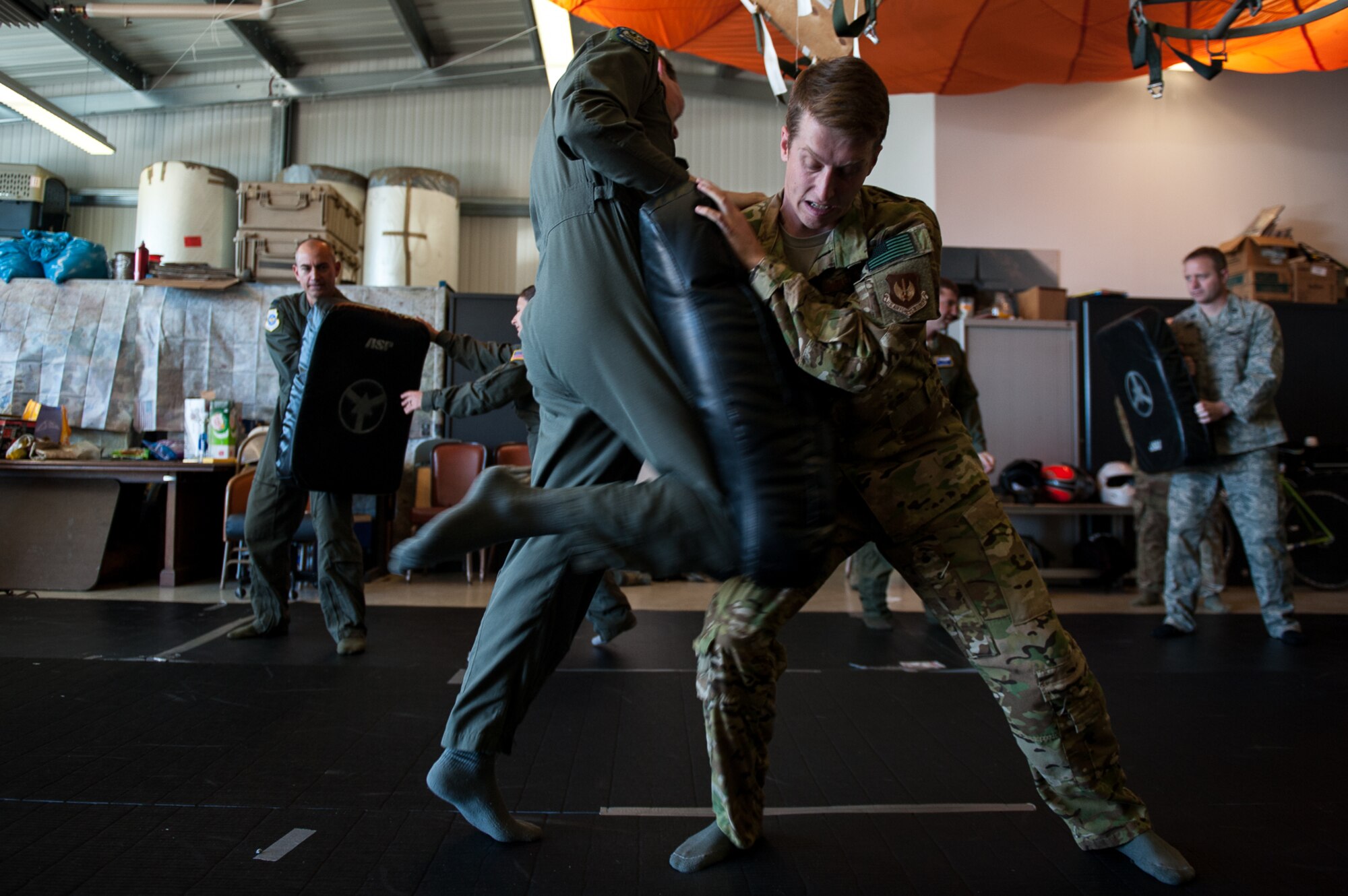 U.S. Air Force Capt. Christopher Comtois, 37th Airlift Squadron pilot, knees a blocking pad while Capt. Kristopher Martin, 37th AS pilot, braces the impact during combat survival training on Ramstein Air Base, Germany, May 10, 2017. Aircrew members took turns practicing combative techniques as part of their Survival Evasion Resistance and Escape refresher course. (U.S. Air Force photo by Senior Airman Devin Boyer/Released)