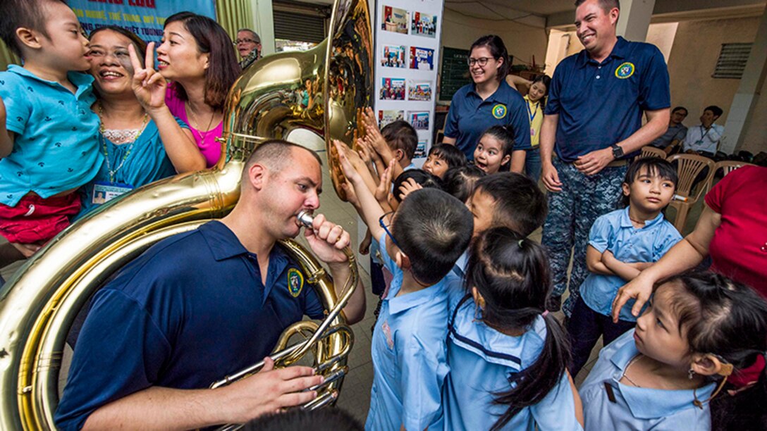 Navy Petty Officer 2nd Class James Brownell plays the tuba for hearing-impaired students as they feel the sound vibrations with their hands.