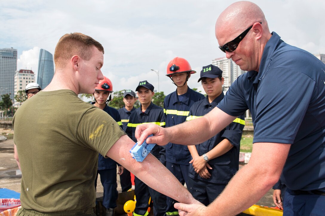 Coast Guard Petty Officer 1st Class Jason Munoz, right, simulates oil contamination removal from Marine Corps Lance Cpl. Austin Buckley as Vietnamese emergency responders observe during a search, rescue and oil spill response field training exercise during Pacific Partnership 2017 in Da Nang, Vietnam, May 13, 2017. Munoz is a Marine Science Technician assigned to the U.S. Coast Guard Pacific Area Incident Management. Buckley is assigned to the 9th Engineer Support Battalion. Navy photo by Petty Officer 2nd Class Joshua Fulton 