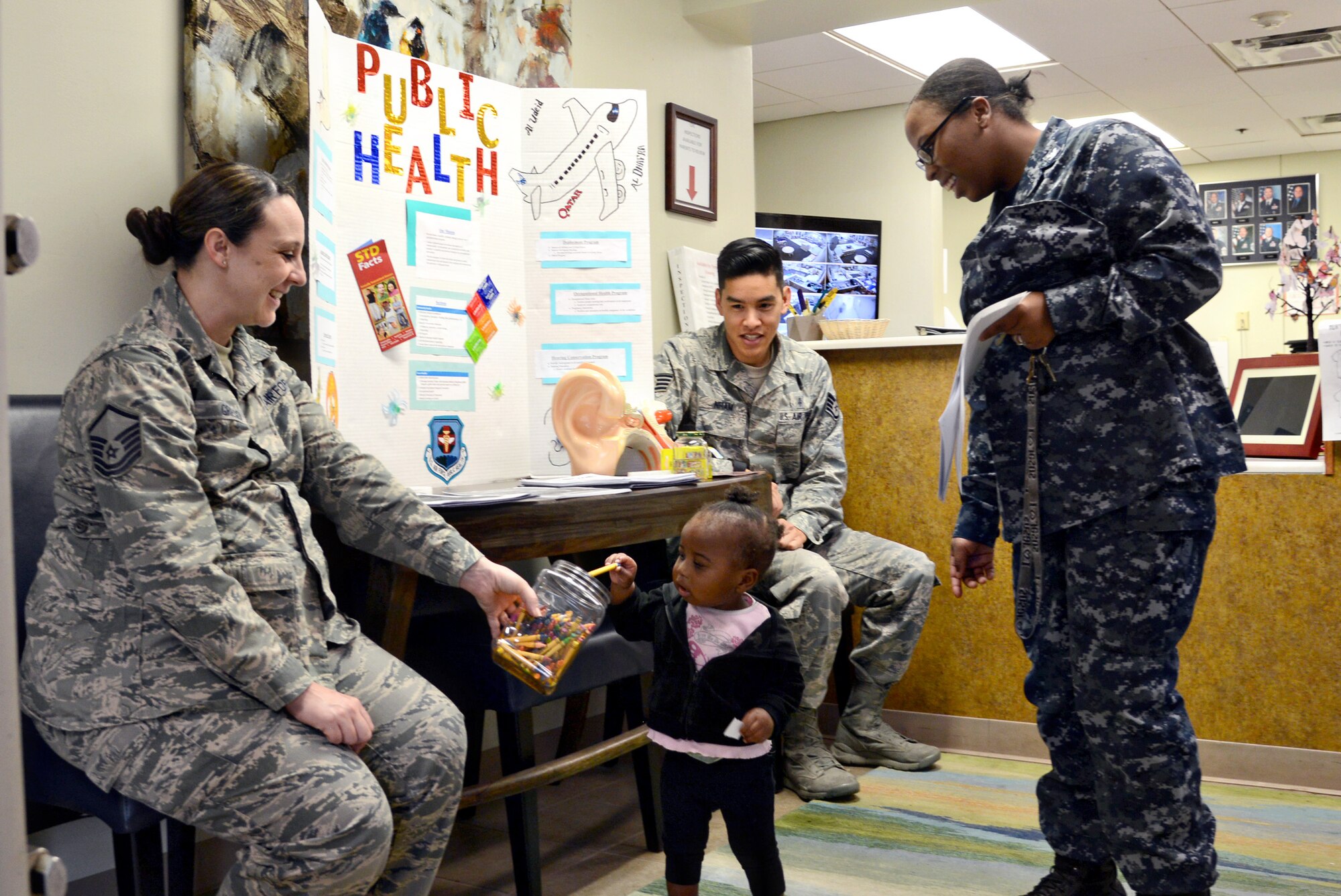 Teziah Davis, 1-year-old, grabs a sticker and crayon from Master Sgt. Tiffany Griego, while her mother, Petty Officer 3rd Class Otisa Williams, with Strategic Communications Wing ONE, and Staff Sgt. Alan Nham, look on. Master Sgt. Griego and Staff Sgt. Nham, both with the 72nd Aerospace Medicine Squadron, handed out goodies and educational materials at the Child Development Center West on April 5 during Public Health Week. (Air Force photo by Kelly White)