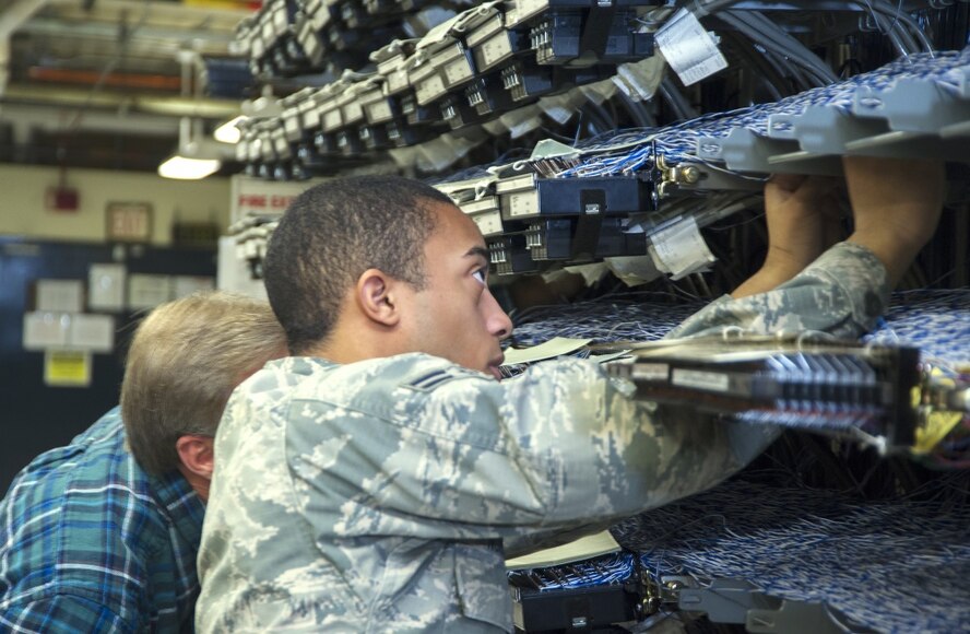 Airman 1st Class Nicklaus Norman, Voice Network System technician, and Doug Vonada, Voice Network Systems chief, trace one of the thousands of phone lines passing through the main distribution frame at Wright-Patterson Air Force Base. The Voice Network Systems team is replacing all the legacy phone systems with Voice over Internet Protocol, a new system accessing phone service through the internet.  (U.S. Air Force Photo/ R.J. Oriez)