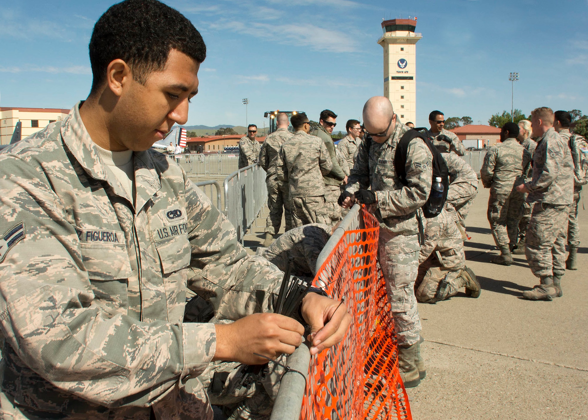 Airman 1st Class Javimeleshe Cruz Figueroa, 860th Aircraft Maintenance Squadron, zip ties netting to temporary fencing surrounding the distinguished visitors section on the flight line May 5, 2017 at Travis Air Force Base, Calif.  Over 100 volunteers set up 2,000 chairs, barriers and temporary fence lines in preparation for the Wings over Solano Air Show.  (U.S. Air Force  photo/T.C. Perkins Jr.)