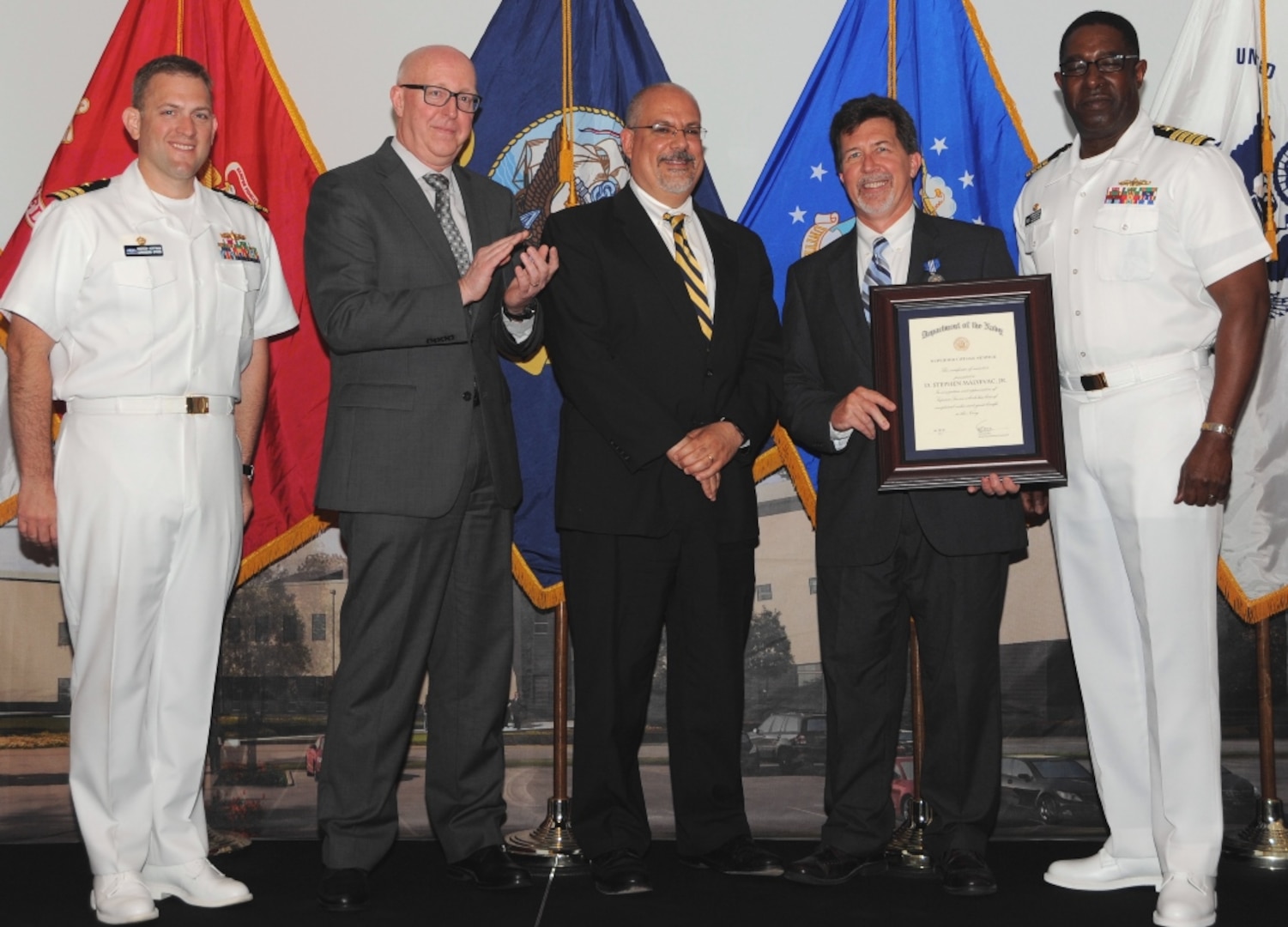 DAHLGREN, Va. (May 17, 2017) - Stephen Malyevac holds a framed certificate moments after receiving the Navy Superior Civilian Service Award at the Naval Surface Warfare Center Dahlgren Division (NSWCDD) Annual Honor Awards ceremony. Malyevac was recognized for numerous technical and leadership contributions as the NSWCDD Distinguished Engineer for Surface Engagement. "His accomplishments as a nationally recognized expert in guidance and control, missile systems, guided projectiles, and surface weapon systems have played a critical role in establishing Dahlgren Division's reputation as a center of excellence for weapon system engineering and integration," according to the citation. "Mr. Malyevac's leadership on numerous high profile technical efforts has resulted in the successful fielding of many of the technologies and capabilities that form the foundation of our surface fleet today."  Standing left to right: Combat Direction Systems Activity Commanding Officer Cmdr. Andrew Hoffman; Naval Surface Warfare Center and Naval Undersea Warfare Center Executive Director Donald McCormack; NSWCDD Technical Director John Fiore; Malyevac; and NSWCDD Commanding Officer Capt. Godfrey 'Gus' Weekes. 