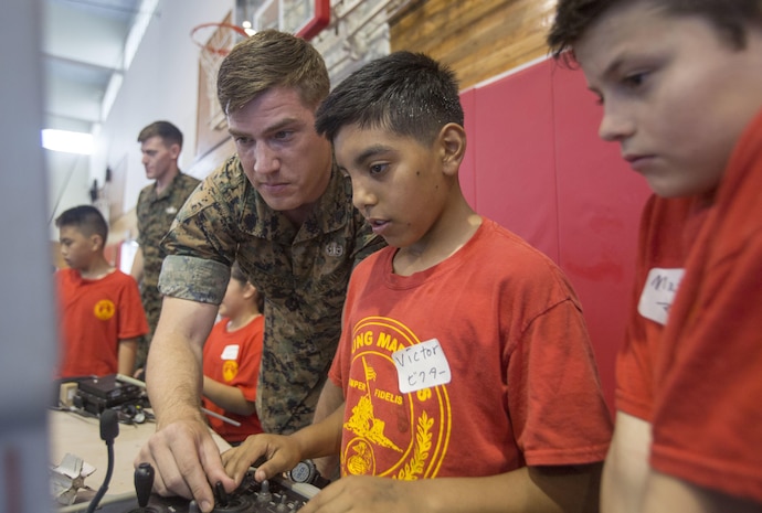 Sgt. Andrew Mattson, an explosive ordnance disposal technician with 3d Maintenance Battalion, 3d Marine Logistics Group, III Marine Expeditionary Force, teaches a child from the Young Marines program how to use the operating control unit to a wireless robot platform used for ordnance disposal during the Young Marines Battalion Field Meet on Camp Hansen, Okinawa, Japan, May 13, 2017. The field meet showcased interactive hands-on displays of various equipment Marines use. (U.S. Marine Corps Photo by Lance Cpl. Deseree Kamm)