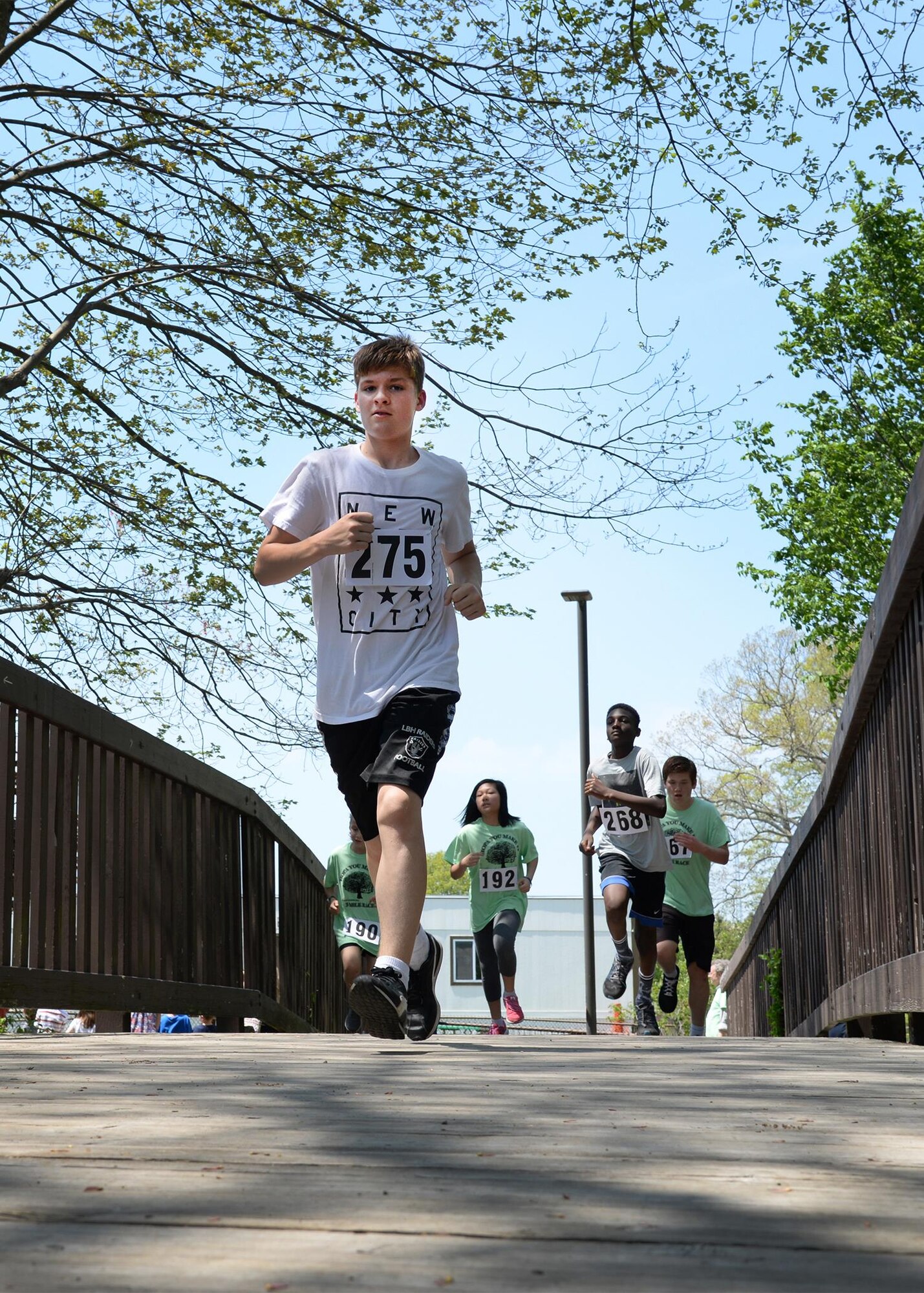 Hayden Santiago, a Hanscom Middle School student, and others run across a bridge during this year's HOPA race at Castle Park on base May 17. The annual three-mile race is named after the Hopa Crabapple tree that was planted near the finish line of the race 32 years ago. (U.S. Air Force photo by Linda LaBonte Britt)