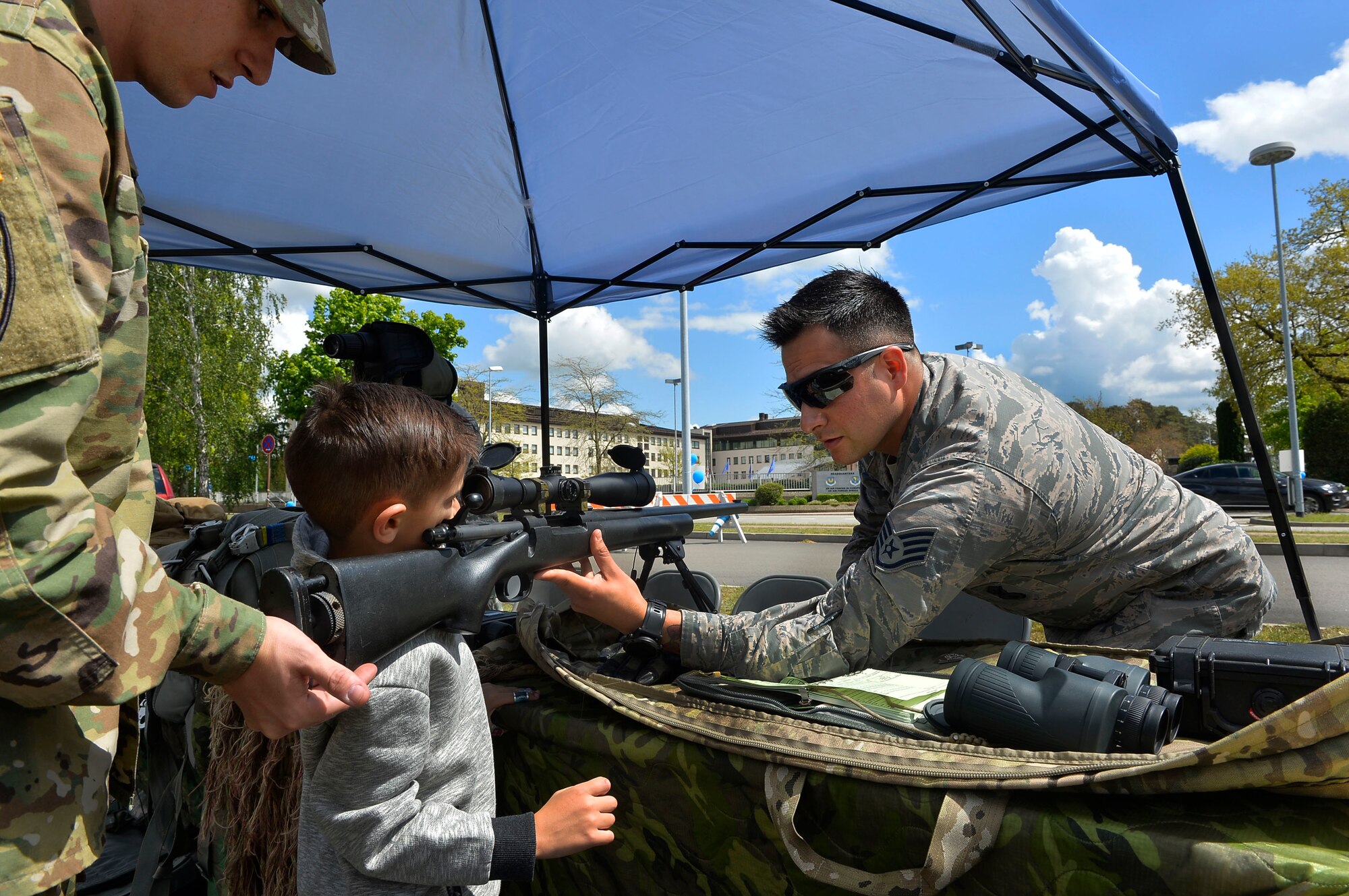 Staff Sgt. Edgar Cerillo, 435th Security Forces Squadron training instructor, far right, helps a child look through the scope of a rifle on Ramstein Air Base, Germany, May 13, 2017. Ramstein conducted a day-long family-friendly police display to kick off Police Week. (U.S. Air Force photo by Airman 1st Class Joshua Magbanua) 