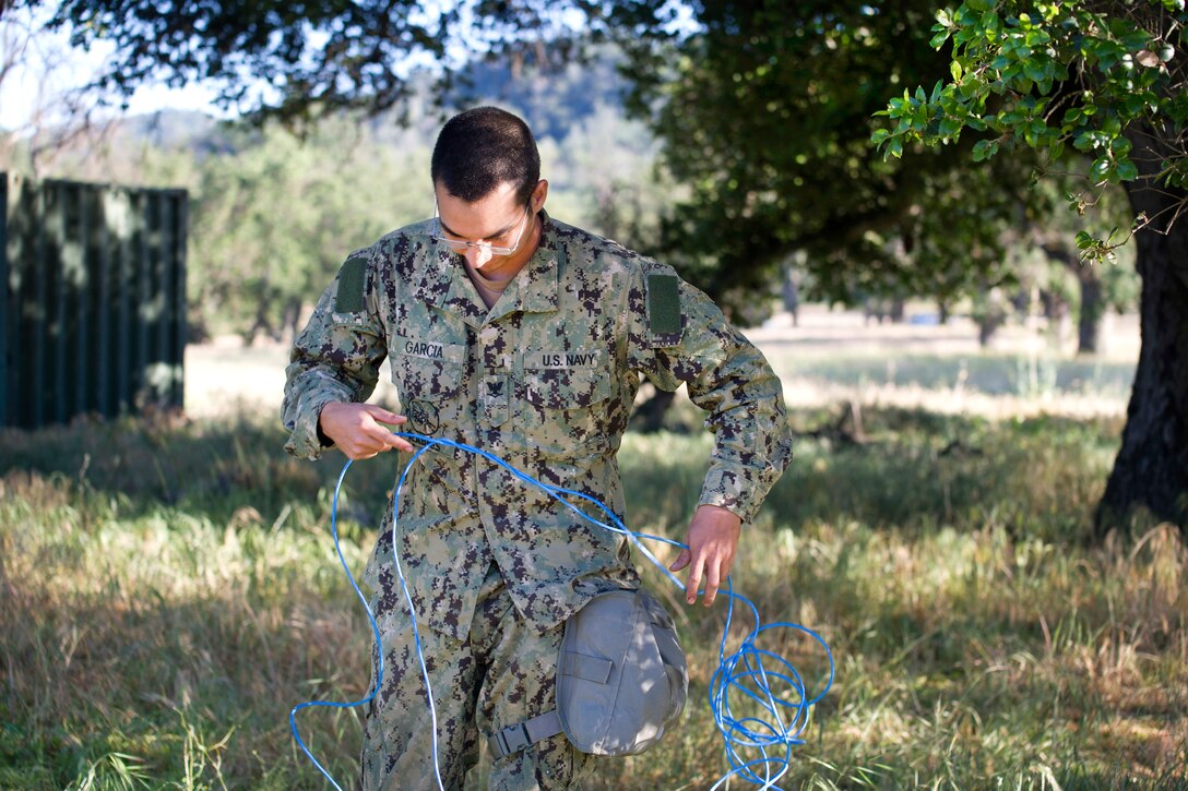 Navy Petty Officer 3rd Class Mark Garcia sets up switch cable wire for communications at a mock forward operating base during a field training exercise at Fort Hunter Liggett, Calif., May 12, 2017. Garcia is an information systems technician assigned to Naval Mobile Construction Battalion 4. Navy photo by Petty Officer 2nd Class Jasmine Flores 