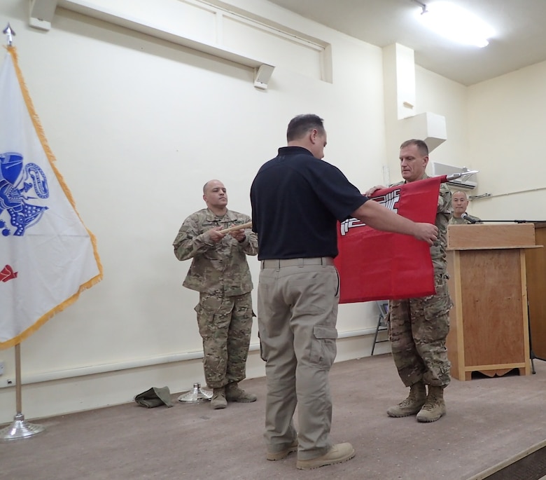 Col. Corey Spencer (right), commander of the U.S. Army Corps of Engineers – Transatlantic Division, Task Force Essayons, unfurls the unit guidon with Mr. Donny Davidson, Task Force Essayons deputy engineer for programs and project management (center), and Master Sgt. Eddie Rodriguez, Kuwait support cell non-commissioned officer-in-charge (left), during the Task Force Essayons activation ceremony, Friday, May 19, 2017 at Camp Taji, Iraq. (Submitted Photo)