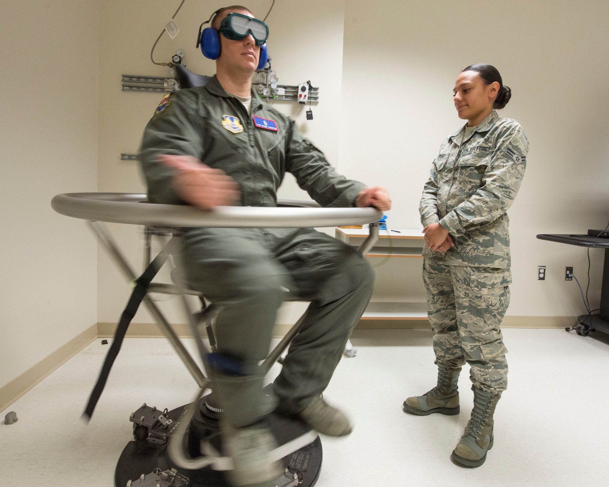 U.S. Air Force Tech. Sgt. Duane Thompson, USAF School of Aerospace Medicine operational physiology technician, spins during a Graveyard Spiral, as part of the Barany chair training for airsickness management program, while Airman 1st Class Agnes Cattaneo, USAF School of Aerospace Medicine operational physiology technician stands-by inside USAFSAM classroom at Wright-Patterson Air Force Base, Ohio, April 26, 2017.  The Barany chair is used as introductory spatial disorientation demonstrator and for rotational training as part of the airsickness management program. (U.S. Air Force photo/Michelle Gigante)