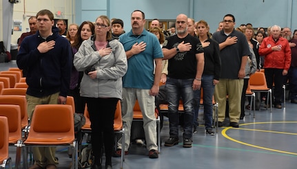 The friends and family of graduating high school seniors who have committed to enlist in the Armed Forces following high school graduation stand while the National Anthem plays during an “Our Community Salutes” event at Fort McCoy, Wisconsin on Armed Forces Day, May 20, 2017.