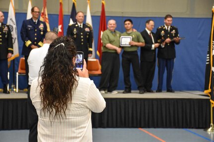 A proud future U.S. Army Reserve mom takes photos as her son receives an "Our Community Salutes" certificate from Medal of Honor recipient Command Sergeant Major (Ret.) Kenneth E. Stumpf and Fort McCoy Senior Commander and 88th Regional Support Command Commanding General, Maj. Gen. Patrick Reinert during an “Our Community Salutes” event at Fort McCoy, Wisconsin on Armed Forces Day, May 20, to recognize and honor graduating high school seniors who have committed to enlist in the Armed Forces following high school graduation.